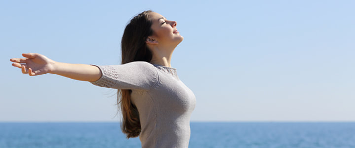 woman with outstretched arms by the ocean on a sunny day